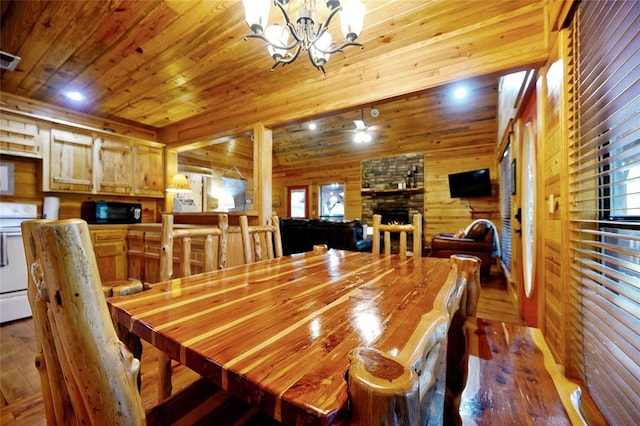 dining space with dark hardwood / wood-style flooring, ceiling fan with notable chandelier, wooden walls, wooden ceiling, and a stone fireplace