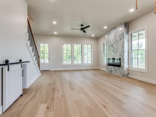 unfurnished living room with a barn door, a premium fireplace, ceiling fan, and light wood-type flooring