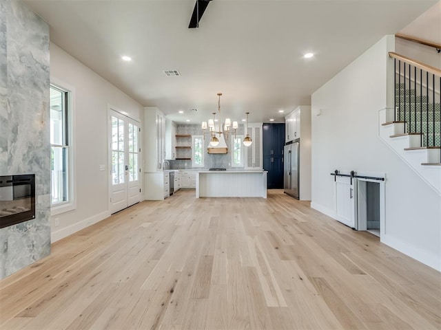 unfurnished living room with a barn door, a chandelier, a fireplace, and light hardwood / wood-style floors