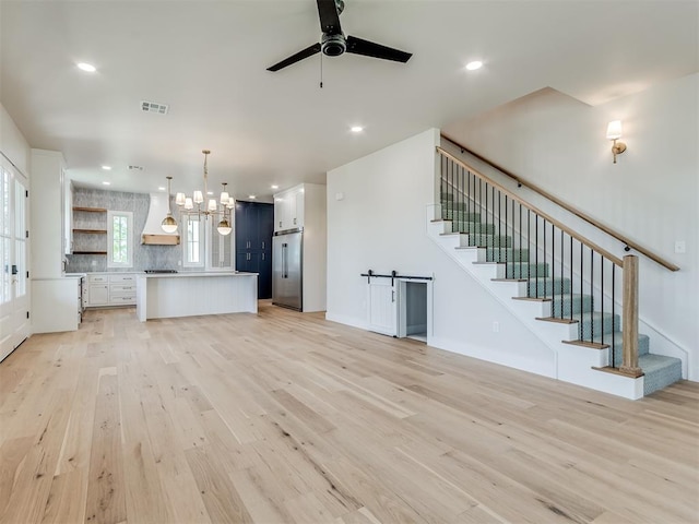 unfurnished living room with ceiling fan with notable chandelier and light wood-type flooring