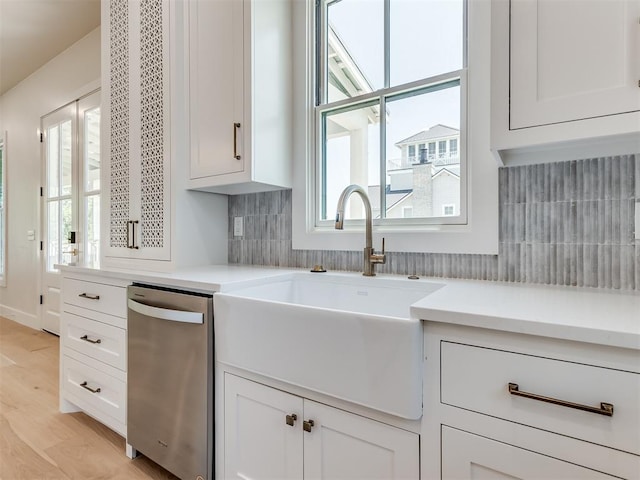 kitchen with white cabinetry, dishwasher, sink, light hardwood / wood-style floors, and decorative backsplash