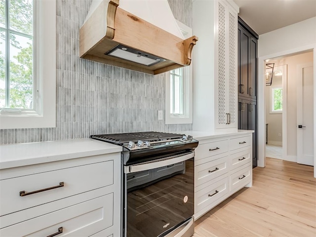 kitchen featuring black stove, light wood-type flooring, plenty of natural light, and custom range hood