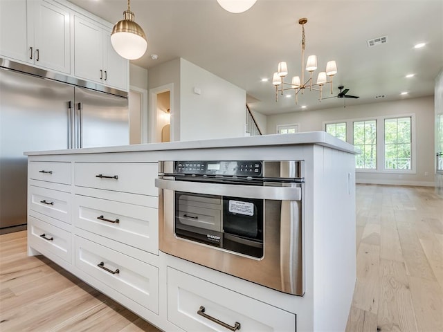 kitchen featuring ceiling fan with notable chandelier, stainless steel appliances, decorative light fixtures, light hardwood / wood-style flooring, and white cabinets