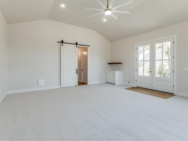 unfurnished living room with lofted ceiling, french doors, ceiling fan, a barn door, and light colored carpet