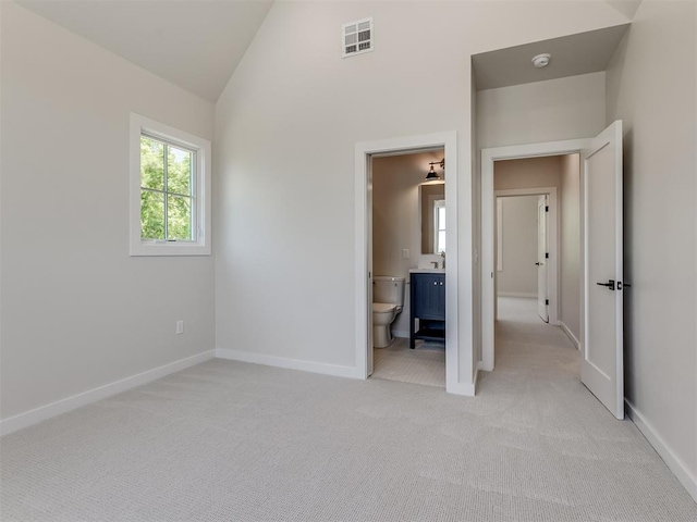 unfurnished bedroom featuring light carpet, ensuite bath, and lofted ceiling