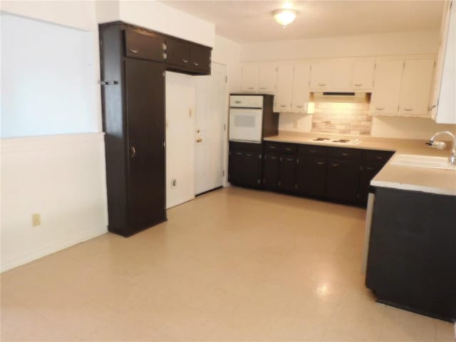 kitchen featuring backsplash, white appliances, white cabinetry, and sink