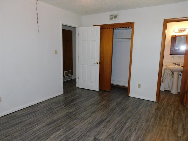 unfurnished bedroom with sink, dark hardwood / wood-style flooring, ensuite bathroom, a textured ceiling, and a closet