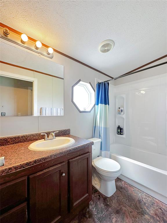 full bathroom with a textured ceiling, toilet, shower / tub combo with curtain, vanity, and ornamental molding