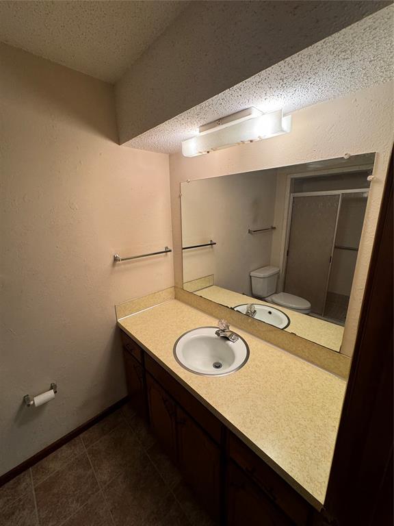 bathroom featuring vanity, tile patterned floors, toilet, a textured ceiling, and walk in shower