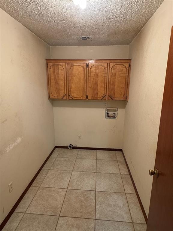 washroom with light tile patterned flooring, cabinets, a textured ceiling, and washer hookup