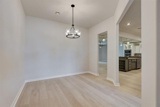 empty room featuring ceiling fan with notable chandelier and light hardwood / wood-style flooring