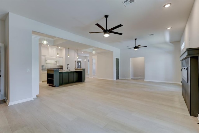 unfurnished living room with ceiling fan, light wood-type flooring, and sink