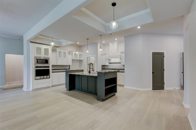 kitchen with white cabinetry, hanging light fixtures, a raised ceiling, a kitchen island with sink, and appliances with stainless steel finishes