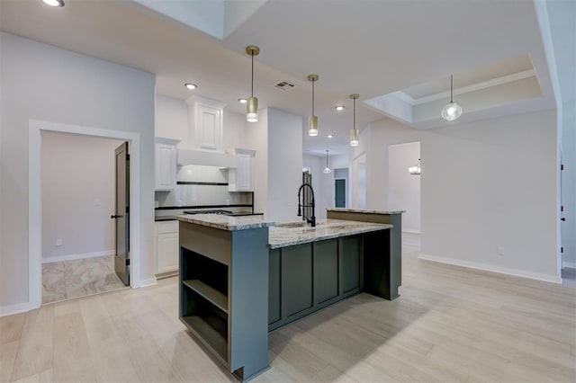 kitchen featuring a kitchen island with sink, white cabinets, light wood-type flooring, light stone countertops, and decorative light fixtures