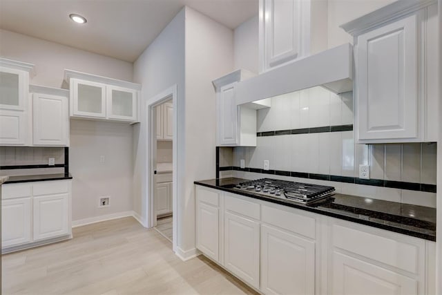 kitchen with white cabinets, stainless steel gas stovetop, light hardwood / wood-style floors, and dark stone countertops