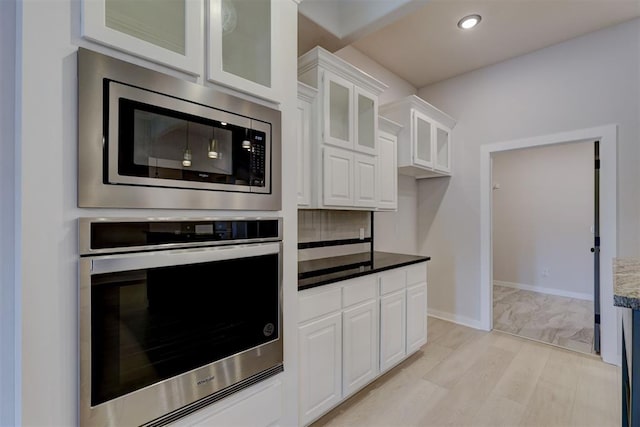 kitchen featuring light hardwood / wood-style flooring, dark stone countertops, tasteful backsplash, white cabinetry, and stainless steel appliances