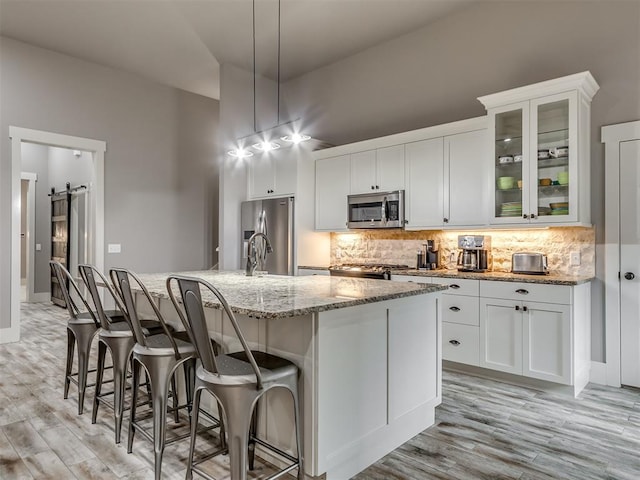 kitchen featuring a barn door, white cabinetry, a center island with sink, and stainless steel appliances