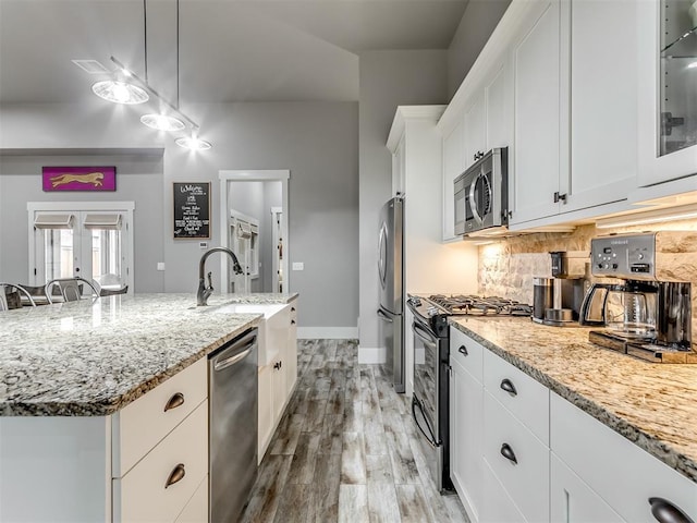 kitchen with a center island with sink, hanging light fixtures, light hardwood / wood-style floors, white cabinetry, and stainless steel appliances