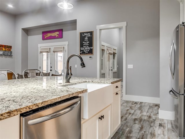 kitchen featuring light stone counters, stainless steel appliances, sink, light hardwood / wood-style floors, and white cabinetry