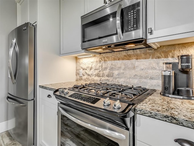 kitchen with decorative backsplash, white cabinets, stainless steel appliances, and light stone counters