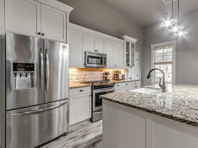 kitchen featuring white cabinets, sink, light stone countertops, appliances with stainless steel finishes, and decorative light fixtures