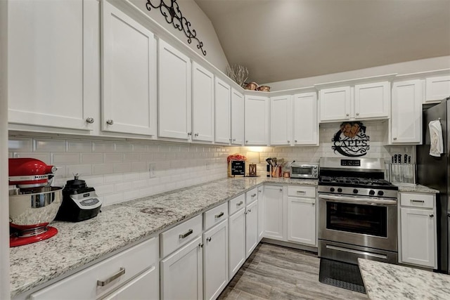 kitchen with stainless steel range with gas cooktop, light stone counters, lofted ceiling, decorative backsplash, and white cabinets