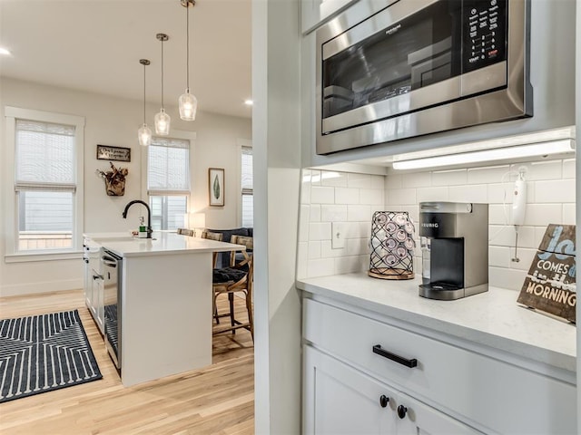 kitchen with tasteful backsplash, decorative light fixtures, light hardwood / wood-style flooring, white cabinetry, and stainless steel microwave