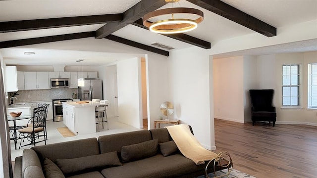 living room featuring vaulted ceiling with beams, light hardwood / wood-style flooring, and sink