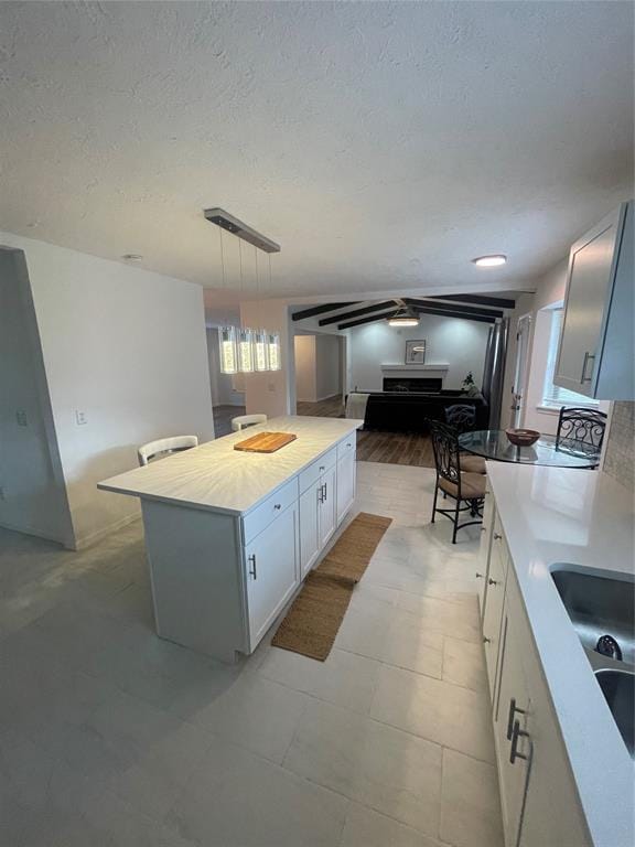 kitchen featuring a textured ceiling, sink, decorative light fixtures, white cabinets, and a center island