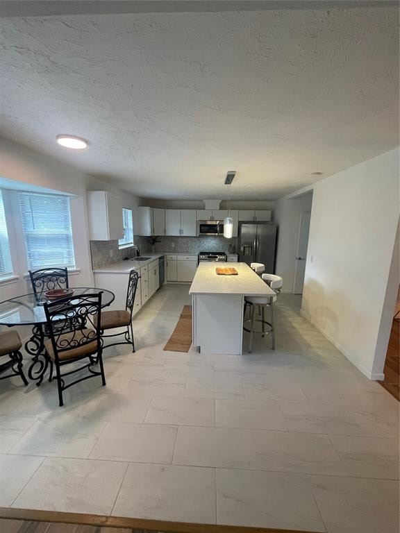 kitchen featuring hanging light fixtures, tasteful backsplash, a kitchen island, a kitchen bar, and stainless steel appliances