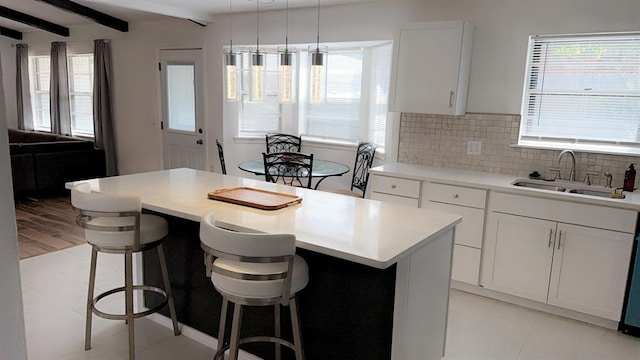 kitchen with beam ceiling, white cabinetry, sink, a center island, and a kitchen breakfast bar