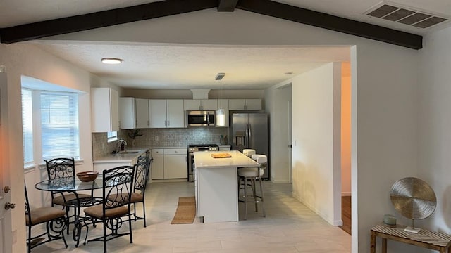 kitchen with white cabinetry, a center island, vaulted ceiling with beams, a kitchen bar, and appliances with stainless steel finishes