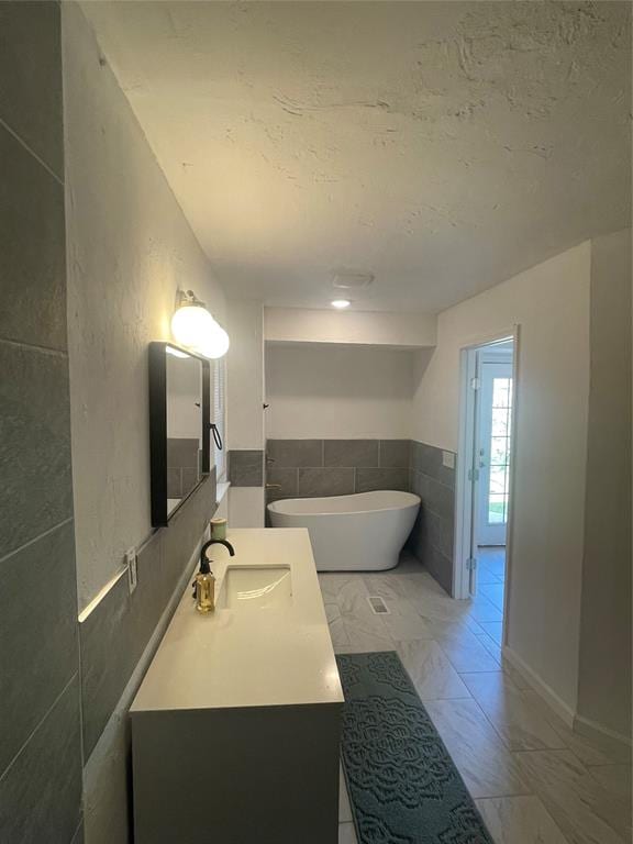 bathroom featuring a tub, vanity, and tile walls