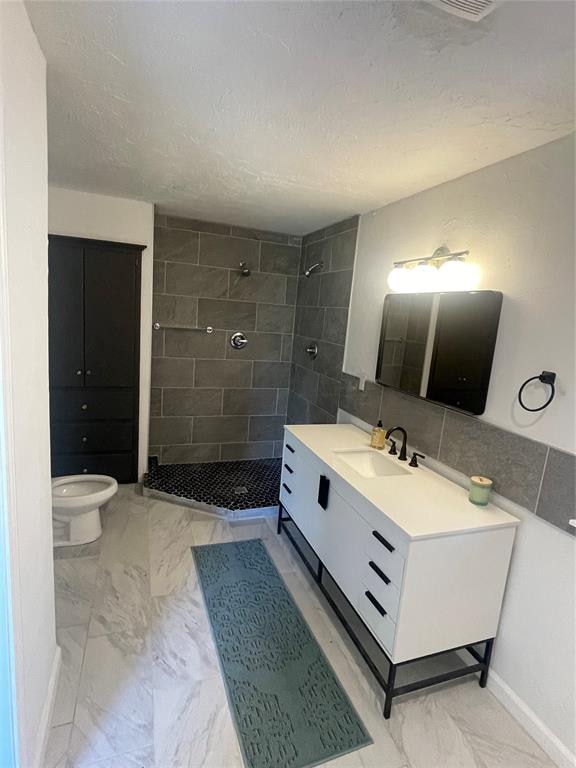 bathroom featuring a tile shower, vanity, a textured ceiling, and toilet