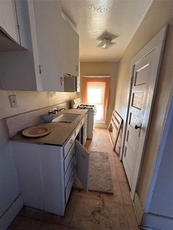 kitchen with white cabinetry, white gas range, sink, and light tile patterned floors