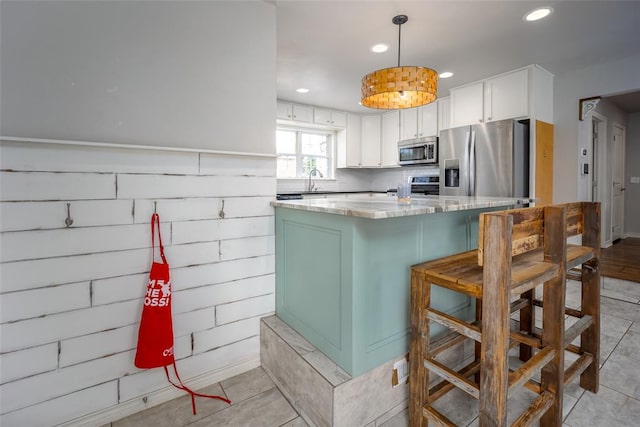 kitchen featuring white cabinetry, hanging light fixtures, stainless steel appliances, a breakfast bar area, and light tile patterned floors