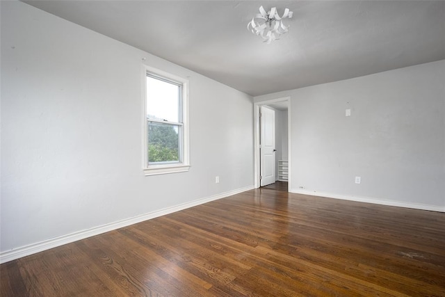 empty room with a notable chandelier and dark wood-type flooring