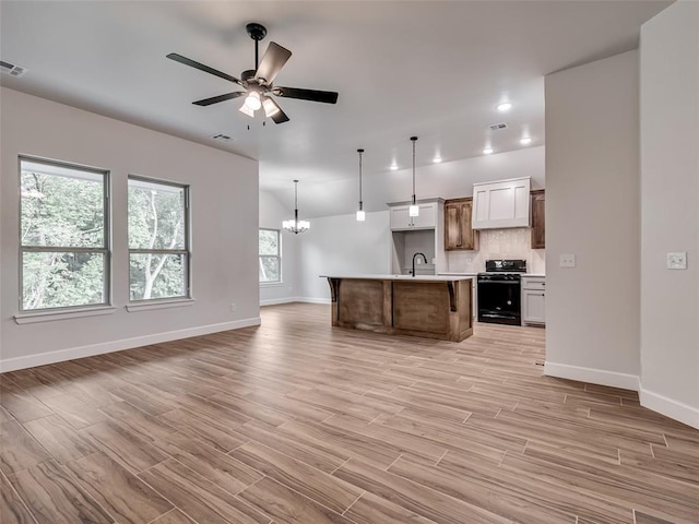 kitchen with light hardwood / wood-style flooring, black / electric stove, an island with sink, decorative light fixtures, and white cabinets