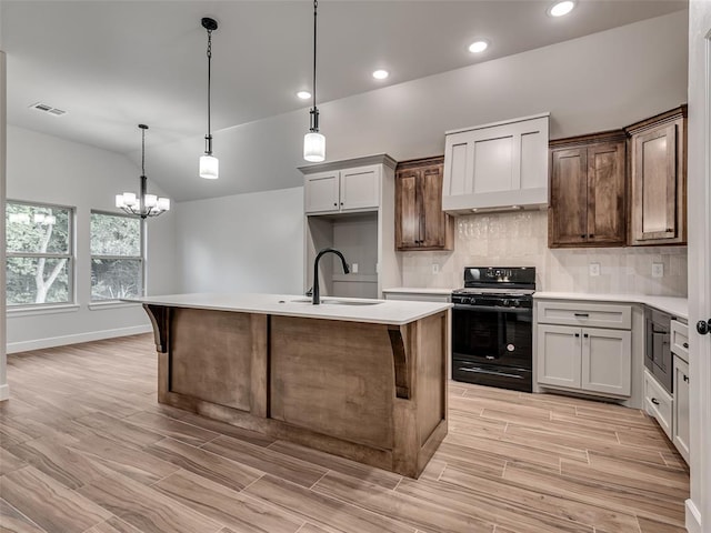 kitchen featuring light wood-type flooring, a kitchen island with sink, sink, pendant lighting, and black gas range