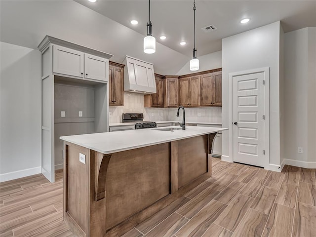 kitchen featuring sink, decorative light fixtures, black gas range, light hardwood / wood-style floors, and an island with sink