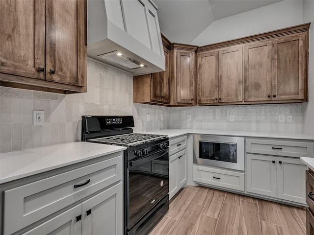 kitchen with stainless steel microwave, backsplash, premium range hood, vaulted ceiling, and gas stove