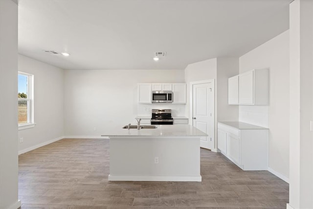 kitchen featuring an island with sink, sink, white cabinets, stainless steel appliances, and light wood-type flooring