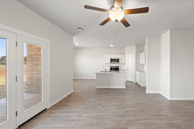 unfurnished living room with ceiling fan, a healthy amount of sunlight, sink, and light wood-type flooring