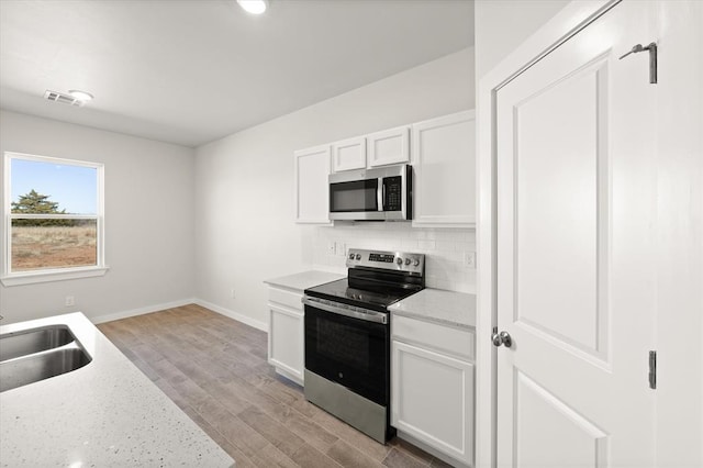 kitchen featuring sink, light hardwood / wood-style flooring, appliances with stainless steel finishes, white cabinetry, and decorative backsplash