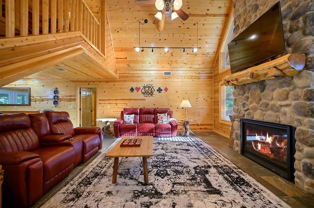 living room with wood walls, high vaulted ceiling, a stone fireplace, ceiling fan, and wood ceiling