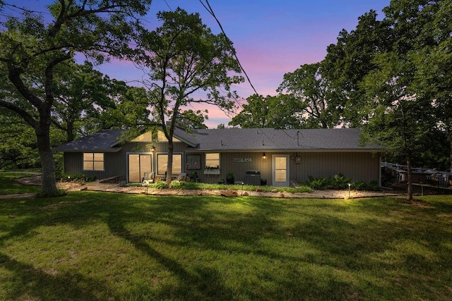 back house at dusk featuring a lawn and cooling unit