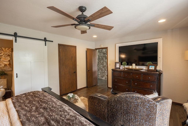 bedroom with ensuite bathroom, a barn door, wood-type flooring, and ceiling fan