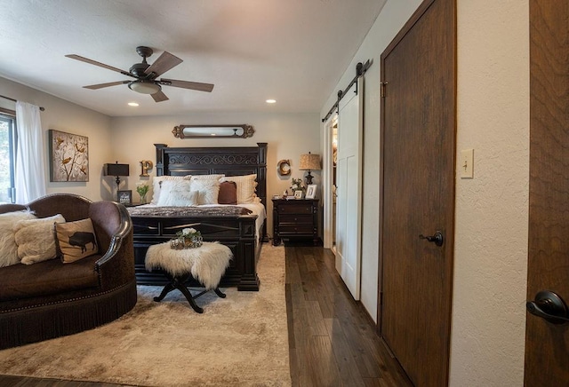 bedroom featuring a barn door, ceiling fan, and dark wood-type flooring