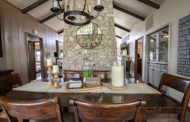 dining space with vaulted ceiling with beams, wood walls, and a chandelier