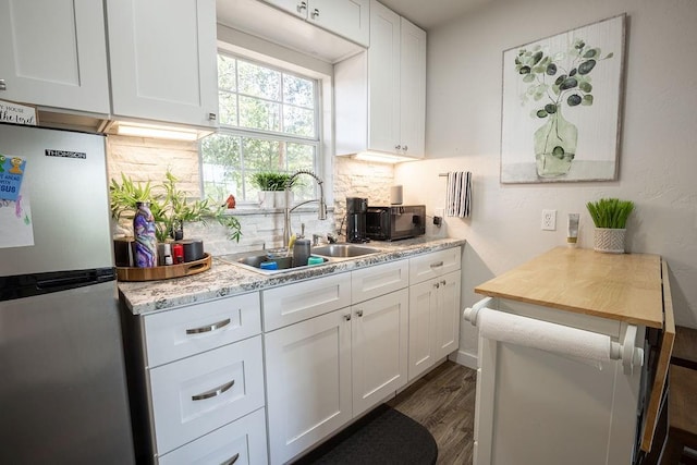 kitchen featuring tasteful backsplash, stainless steel refrigerator, white cabinetry, and sink